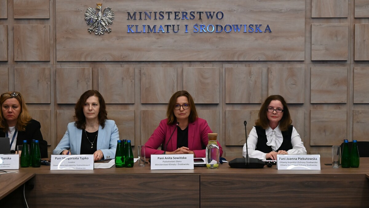 widoczne cztery kobiety elegancko ubrane, siedzące obok siebie przy długim stole, przed każdą z kobiet ustawiona jest tabliczka informacyjna, w tle napis "Ministerstwo Klimatu i Środowiska"