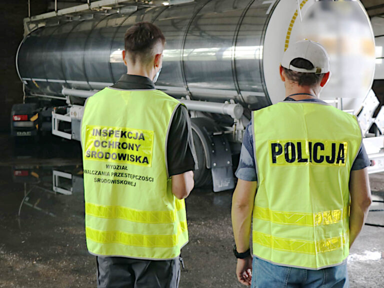 Inspektor Wydziału Zwalczania Przestępczości Środowiskowej WIOŚ we Wrocławiu wraz z funkcjonariuszem Policji stojący tyłem do obiektywu. W tle widać tył cysterny zaparkowanej w hali.